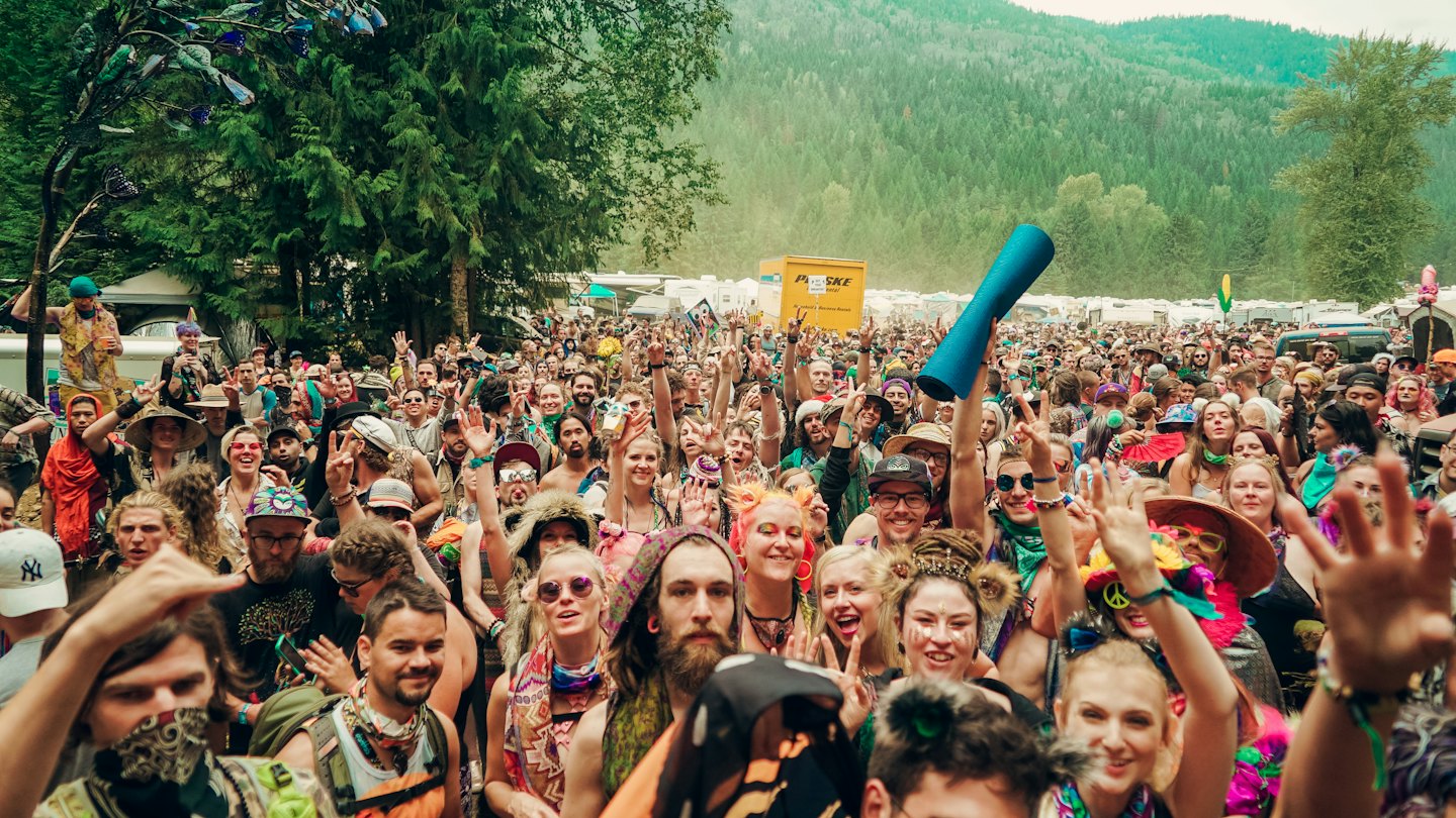 Crowd of happy people cheering with hands up at an outdoor festival.