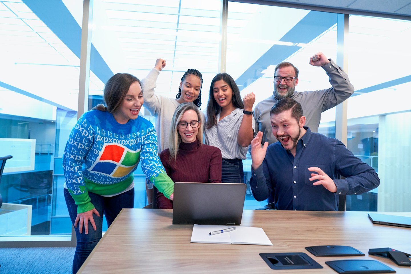 Professionals celebrating around a laptop on an office conference table.